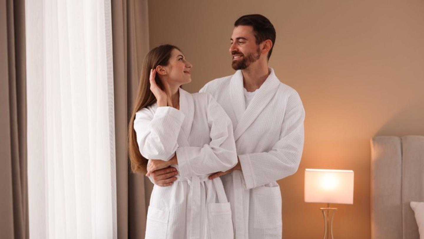 Una pareja en batas blancas, en una habitación de hotel.